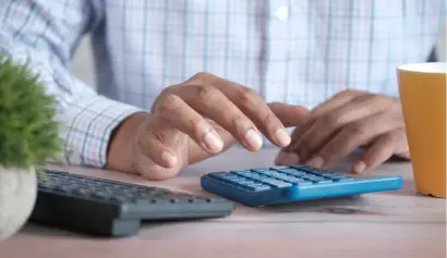 A person using a calculator next to a keyboard and a coffee cup on a wooden desk, focusing on financial calculations.